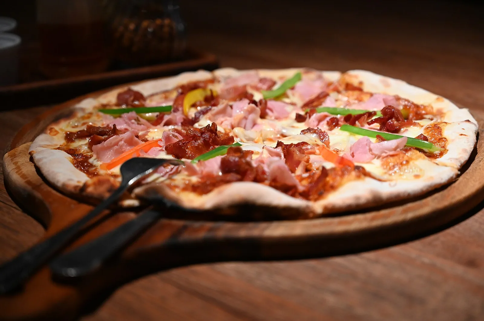 A wood-fired pizza topped with ham, bacon and peppers on a wooden board. The photo was not taken at a Norfolk restaurant.